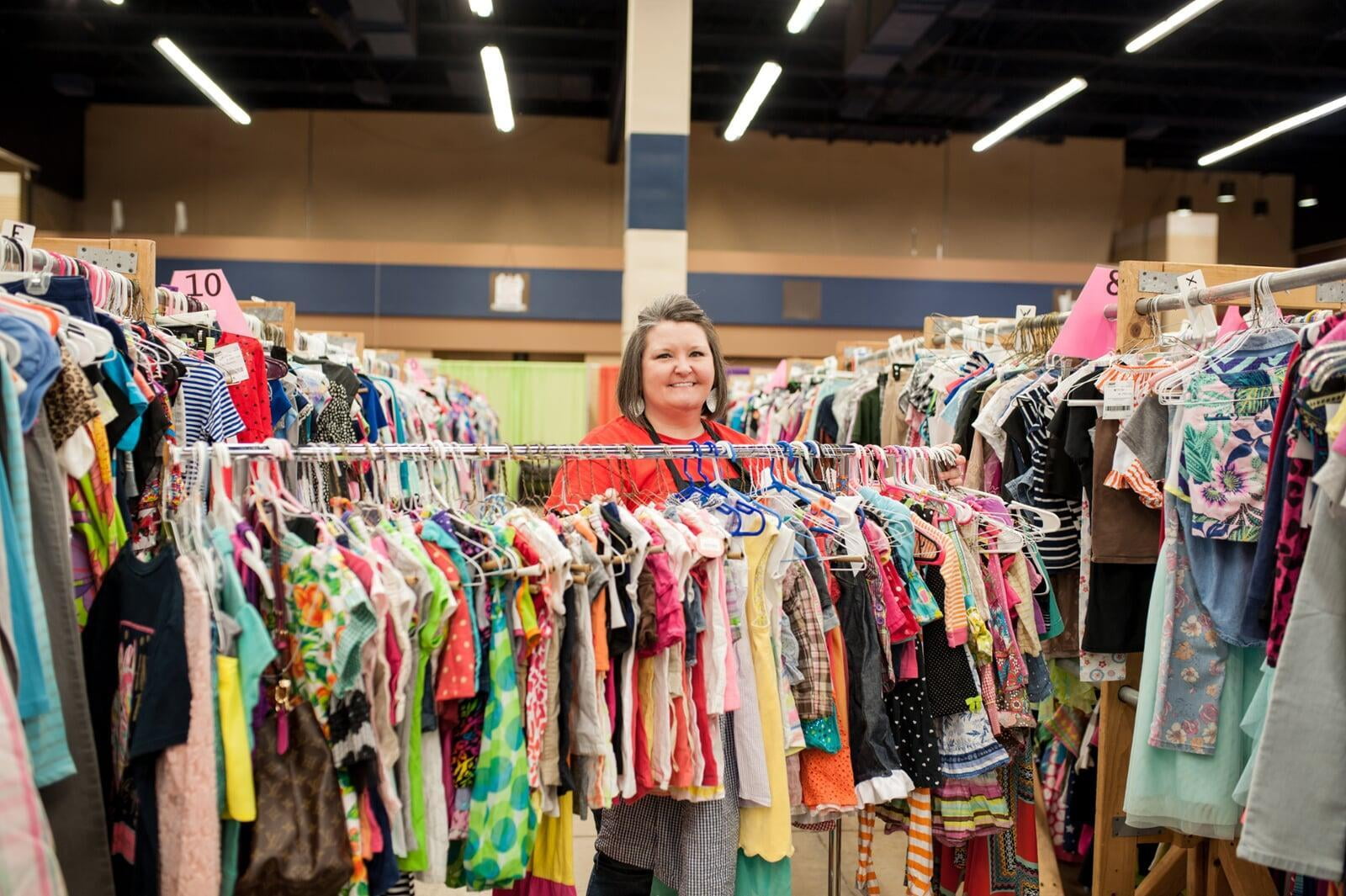 A smiling Team Member stands behind a rack of toddler girl's clothing at the sale.